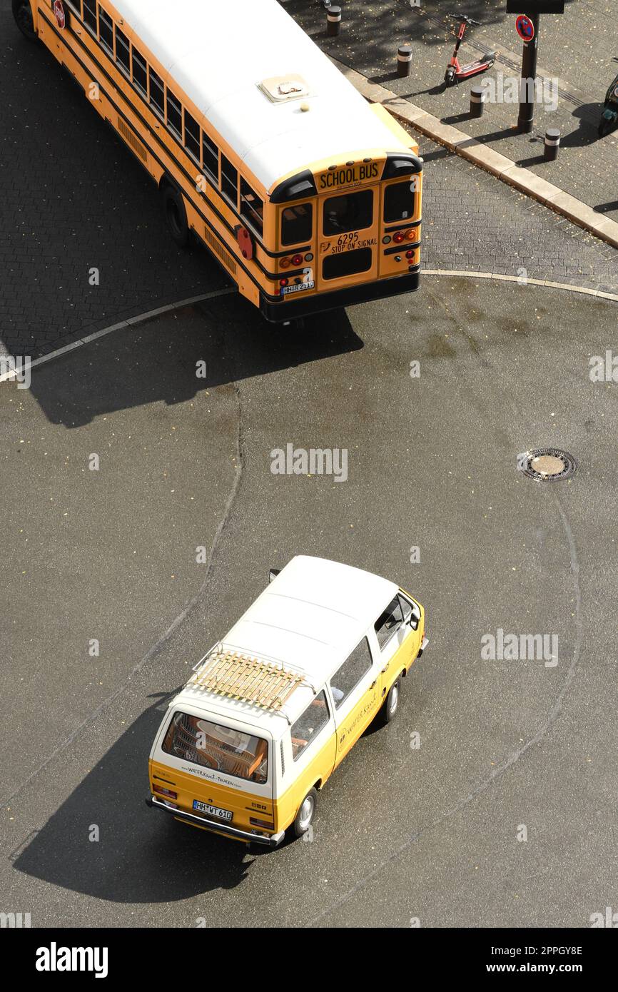 Vertical shot of a yellow and white automobile driving behind an American school bus on a roadway Stock Photo