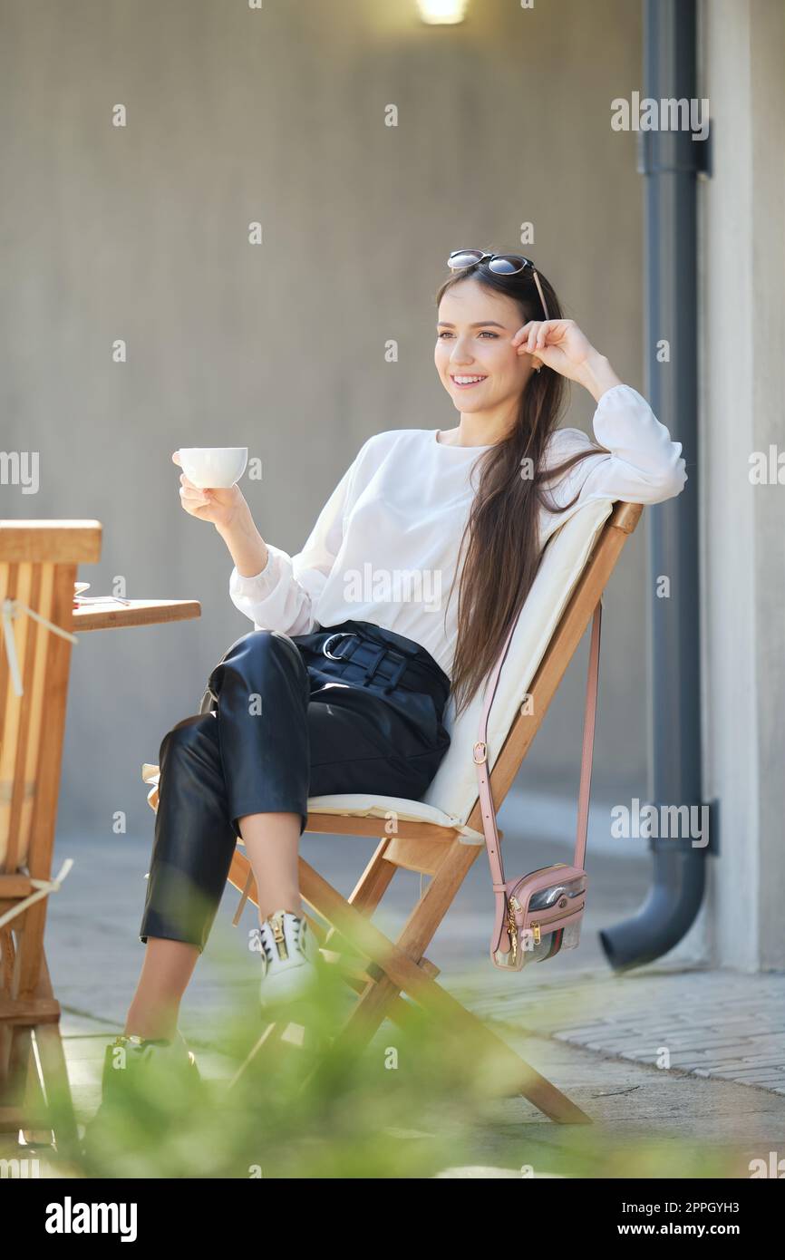 Young woman sitting on the terrace of the cafe in sunny day and ...