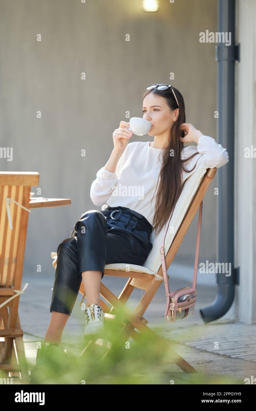 Young woman sitting on the terrace of the cafe in sunny day and ...
