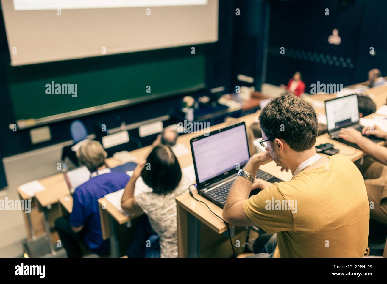 Workshop at university. Rear view of students sitting and listening in lecture hall doing practical tasks on their laptops Stock Photo