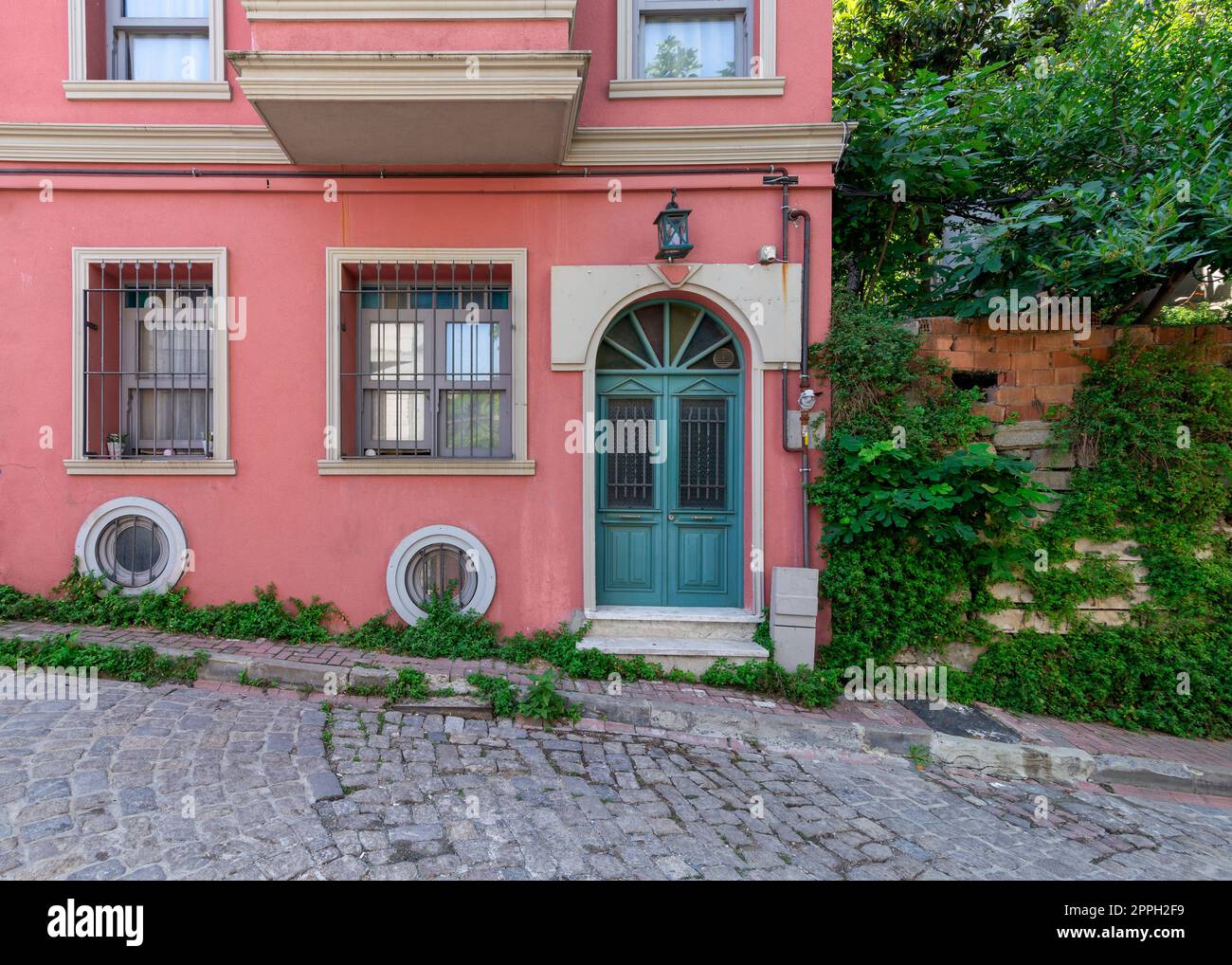 Old house painted in orange, wrought iron windows, and trees, at a cobblestone street, Balat district, Istanbul, Turkey Stock Photo