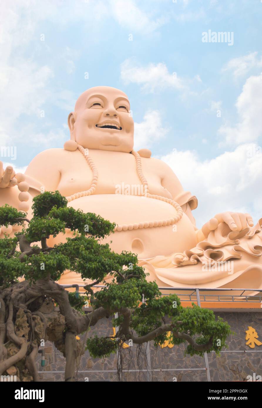 Laughing buddha statue at Vinh Trang temple, near My Tho, Vietnam. Low angle view with bonsai tree on the foreground. Stock Photo