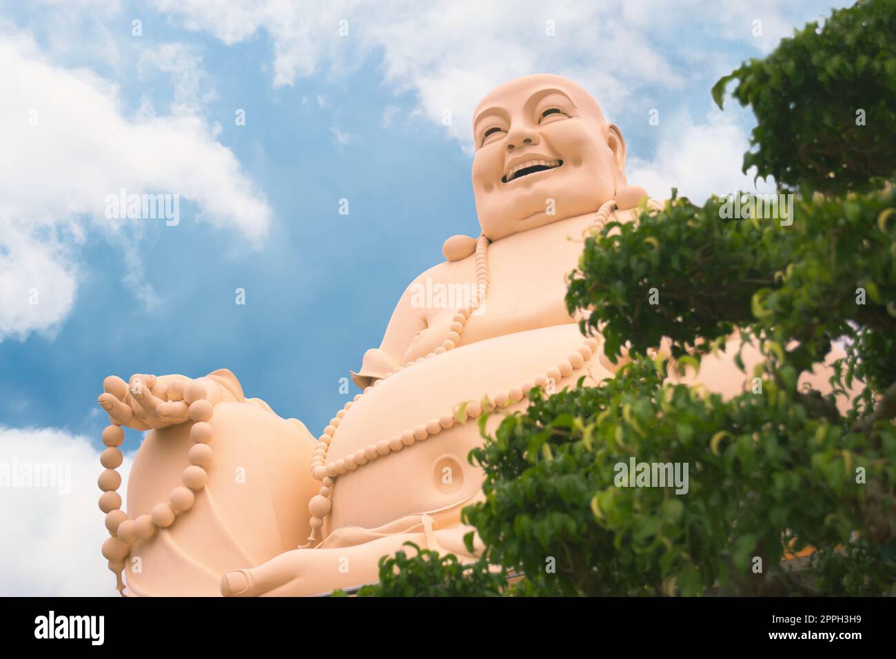 Laughing buddha statue at Vinh Trang temple, near My Tho, Vietnam. Low angle view with bonsai tree on the foreground. Stock Photo
