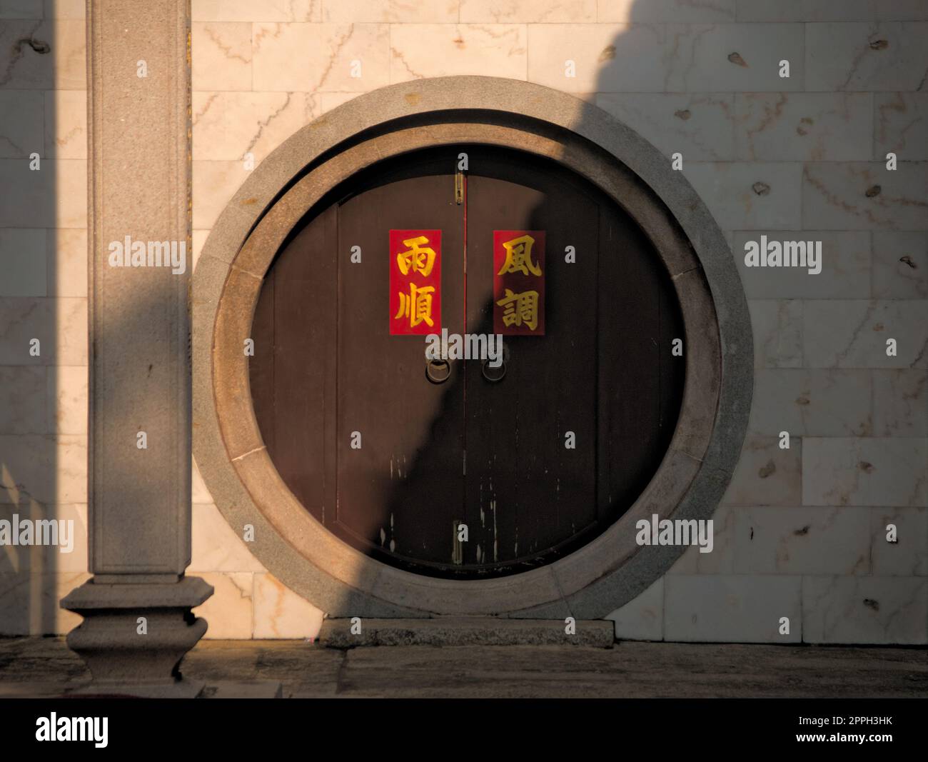 Circular door at a chinese buddhist temple in Saigon, Vietnam. The door is cut in half by light and shadow. The chinese writing says 'Rain' and 'Wind' Stock Photo
