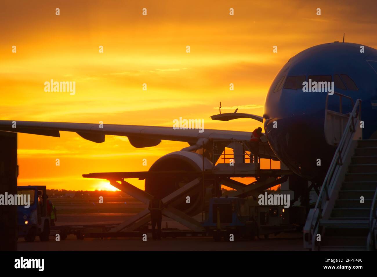 Airport ground crew loading cargo and luggage on a commercial aircraft at dawn. Stock Photo