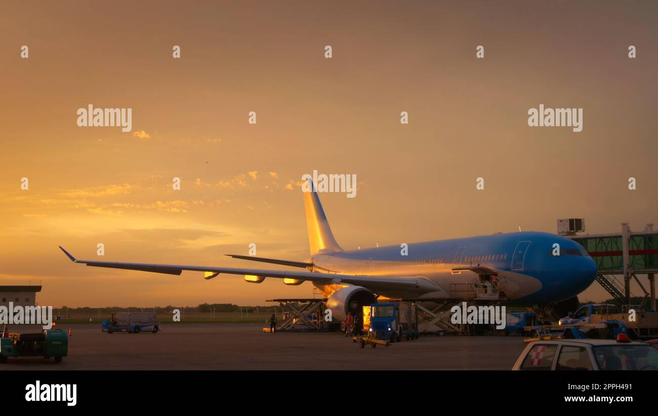 Airport ground crew loading cargo and luggage on a commercial aircraft at dawn. Stock Photo