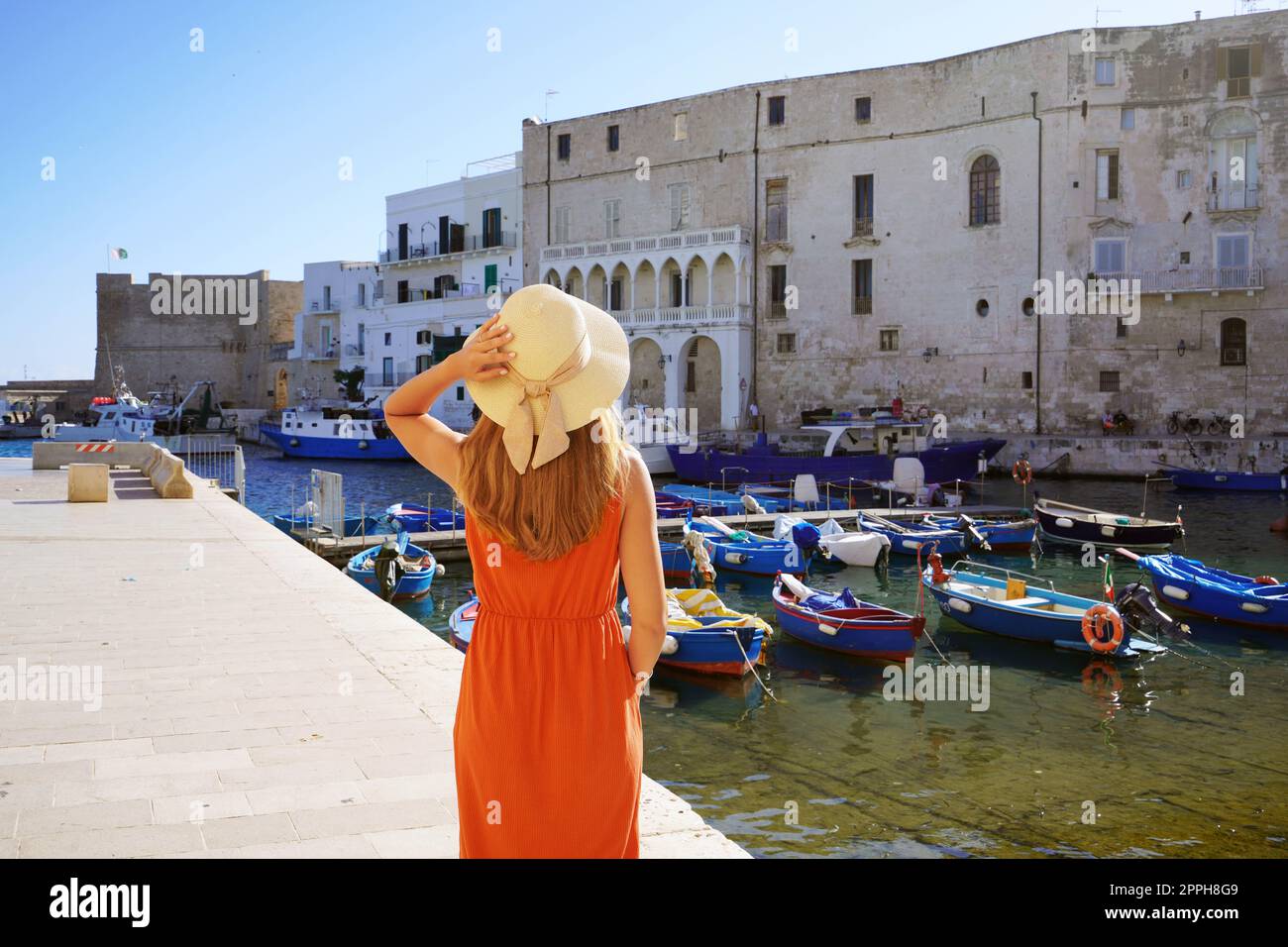 Holidays in Apulia, Italy. Back view of beautiful fashion girl enjoying view of Monopoli ancient port in Apulia, Italy. Summer vacation in Europe. Stock Photo