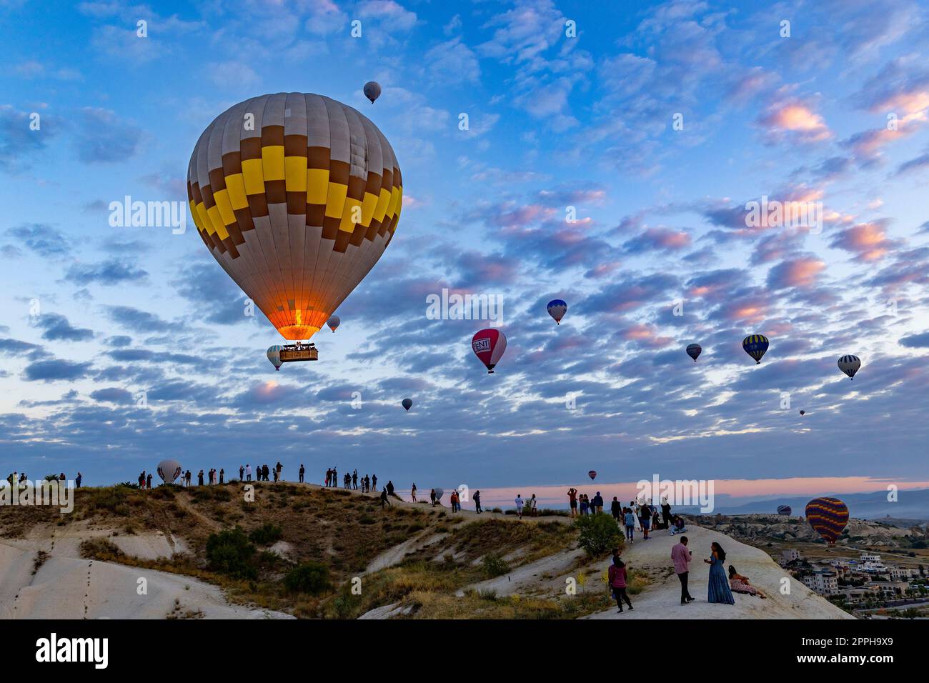 dozens of tourists observe and photograph the spectacle of the hot air balloons over goreme Stock Photo