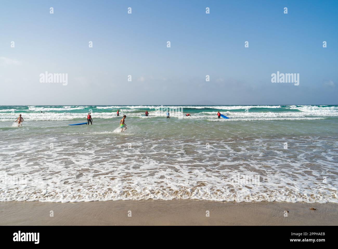 FAMARA BEACH LANZAROTE, CANARY ISLANDS - JULY 21, 2022: Surfers on the waves. Famara Beach (Playa de Famara), popular surfing beach in Lanzarote. Stock Photo