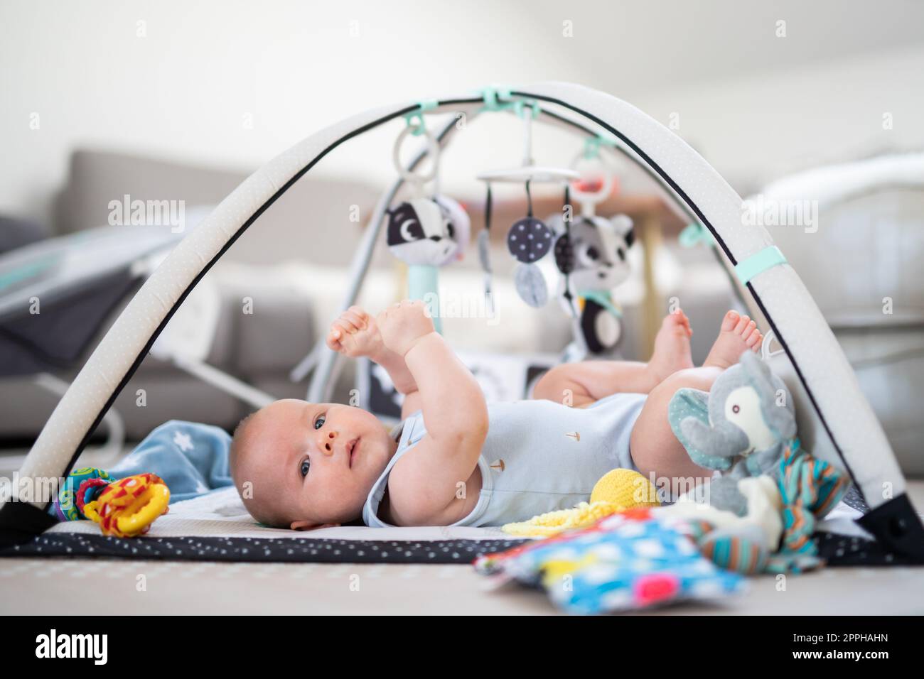 Cute baby boy playing with hanging toys arch on mat at home Baby activity and play center for early infant development. Baby playing at home Stock Photo