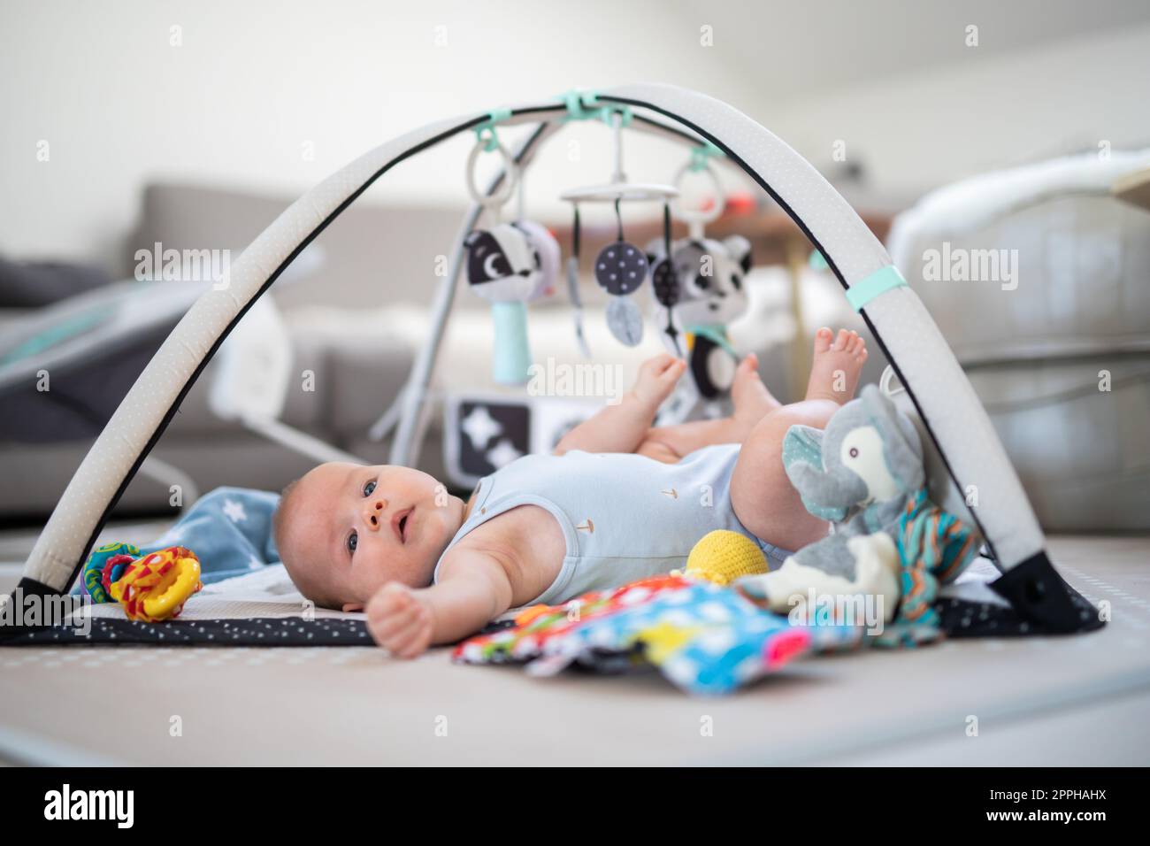 Cute baby boy playing with hanging toys arch on mat at home Baby activity and play center for early infant development. Baby playing at home Stock Photo