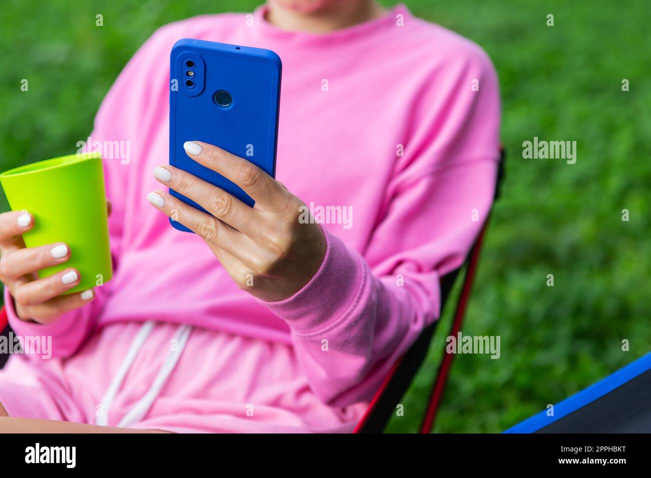 Young female freelancer all in pink sitting on a chair outdoors, relaxing, using smartphone for work. The concept of remote work. Stock Photo