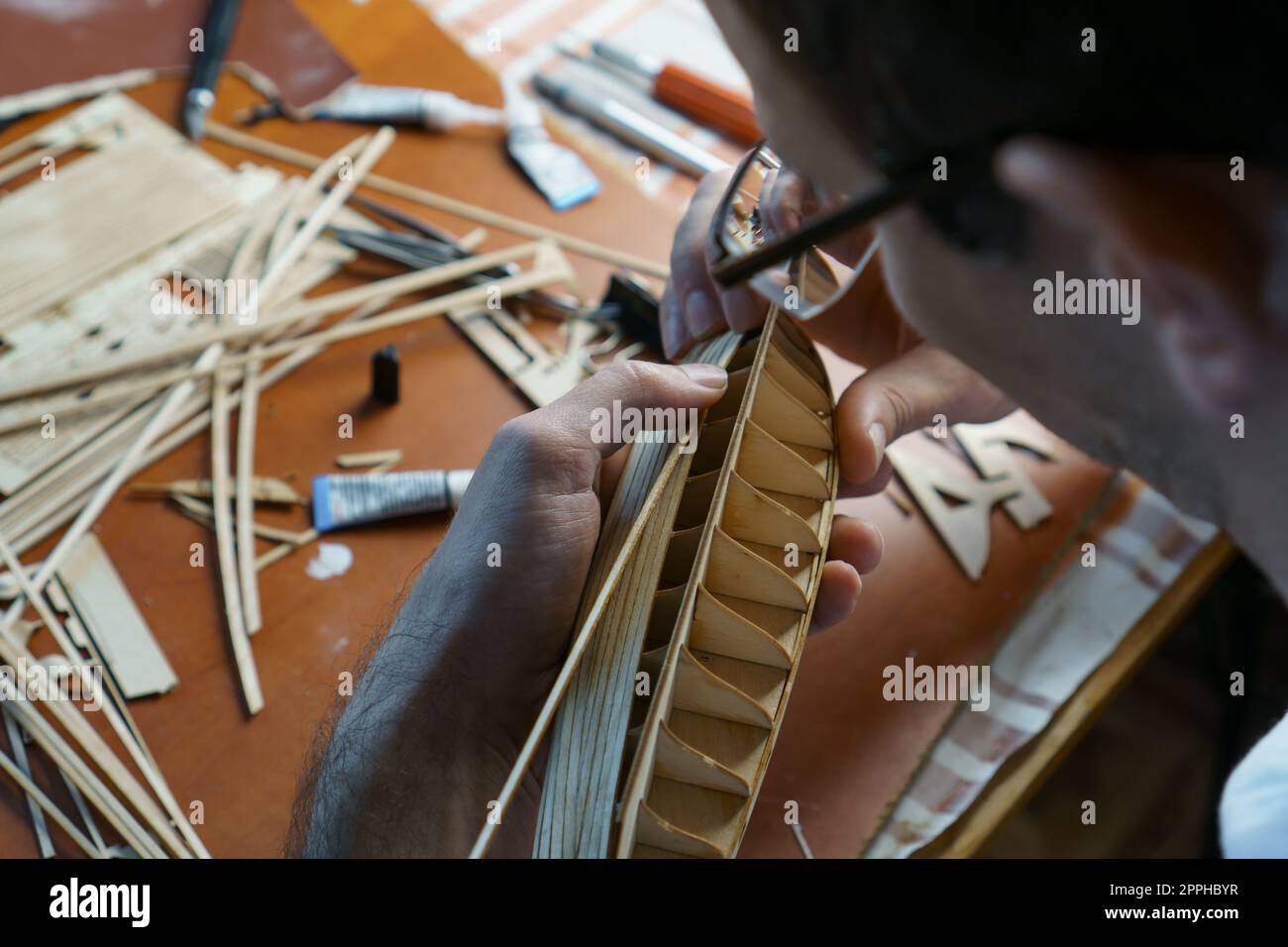 Hands of man gluing plywood details for ship model with glue, holding
