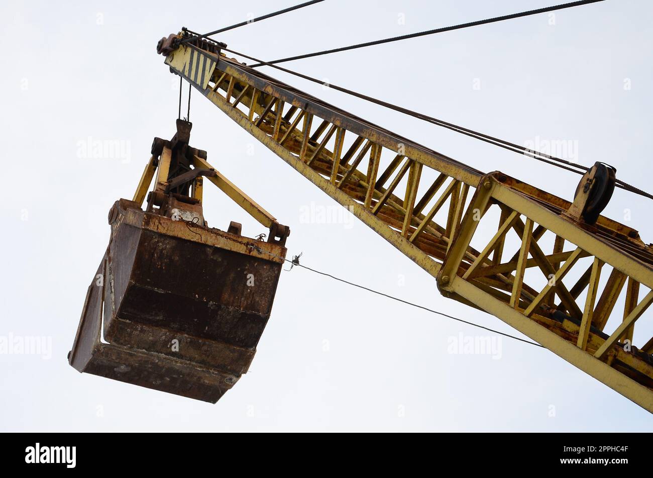 Old yellow mechanical clamshell grab on blue sky background Stock Photo
