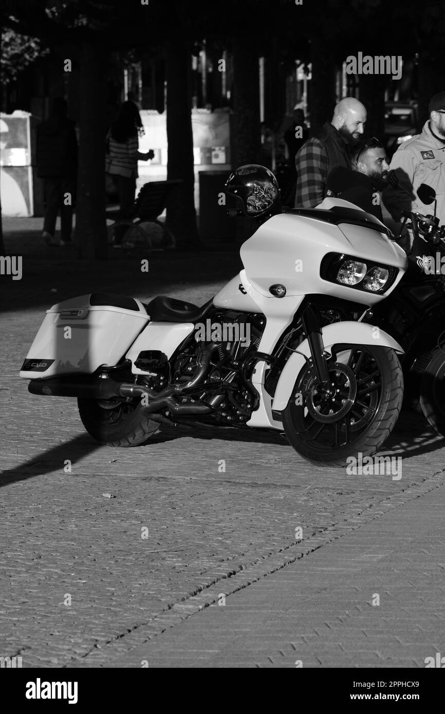 A vertical grayscale of three male standing by a white chopper motorcycle. Harley Davidon in Duesseldorf, Germany. Stock Photo