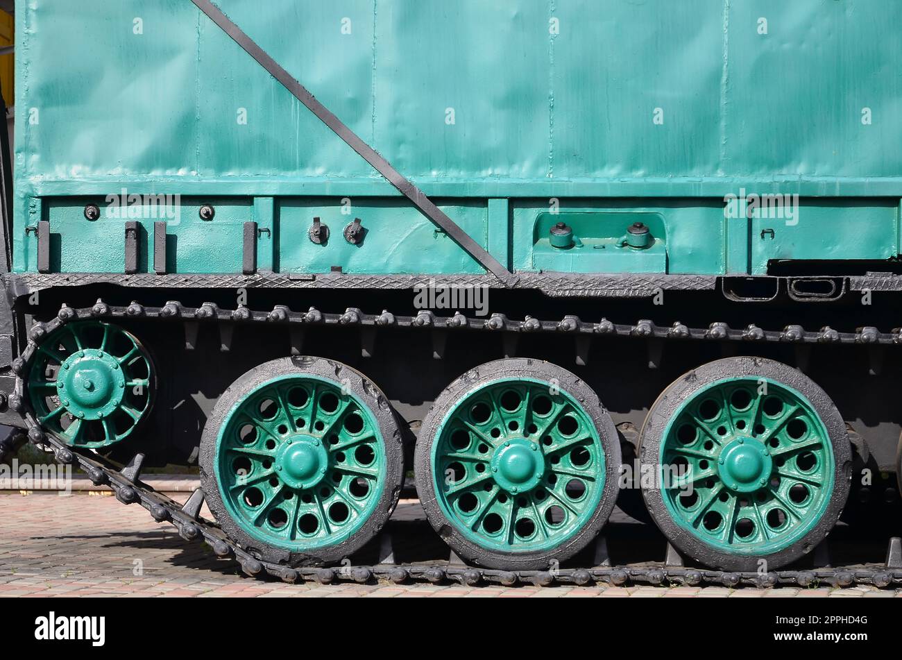 Side view of the vehicle on a caterpillar track with black tracks and green wheels and a side metal wall Stock Photo