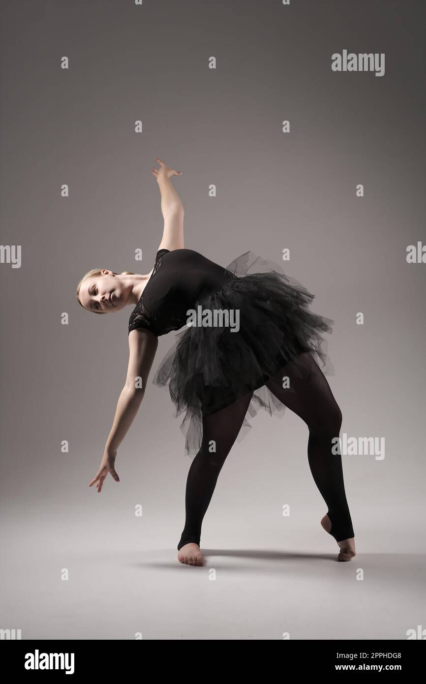 Ballerina Dancing with tutu Modern Ballet Dancer in dancer tutu, Gray Background. Dancer in Black clothes showing her flexibility posing on gray background in studio Stock Photo