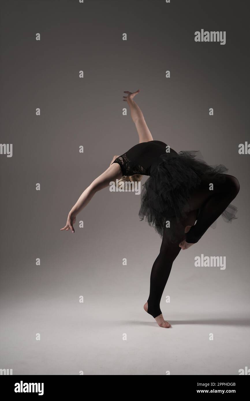 Ballerina Dancing with tutu Modern Ballet Dancer in dancer tutu, Gray Background. Dancer in Black clothes showing her flexibility posing on gray background in studio Stock Photo