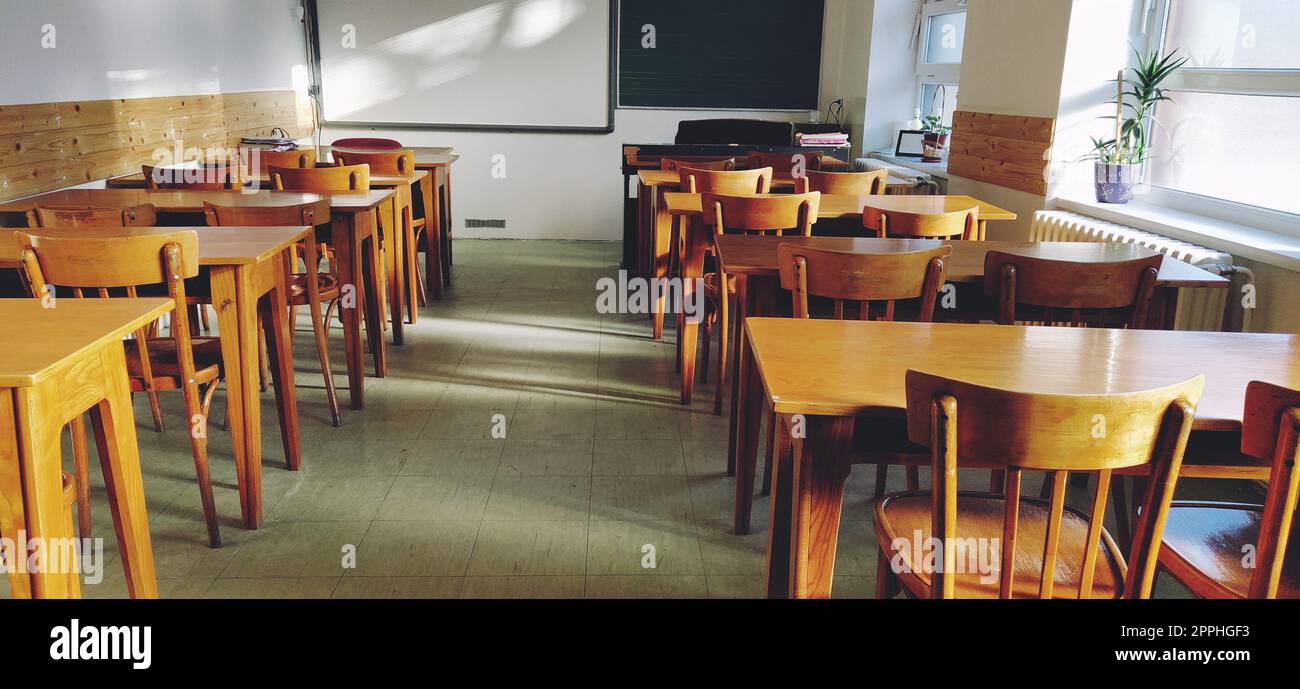 Music solfeggio empty class at school. The sun's rays fall on the floor through the window. Wooden student tables and chairs. School board and white walls. School interior. Stock Photo