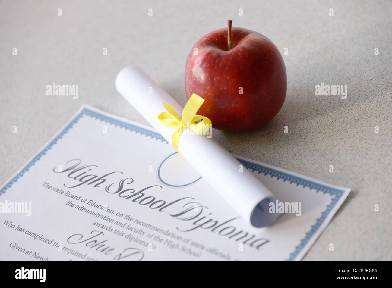 A high school diploma lies on table with small scroll and red apple. Education documents Stock Photo