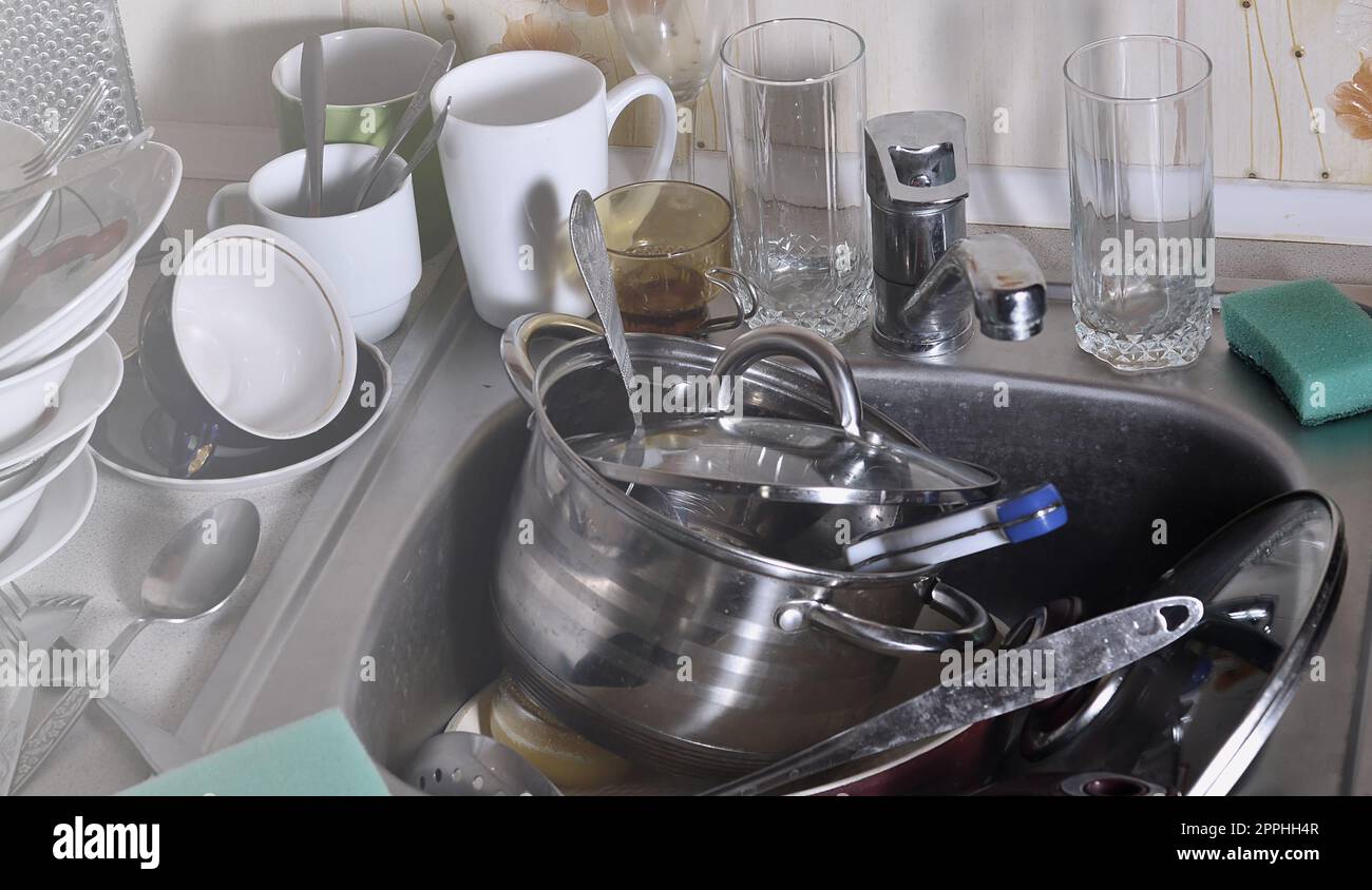 A huge pile of unwashed dishes in the kitchen sink and on the countertop Stock Photo