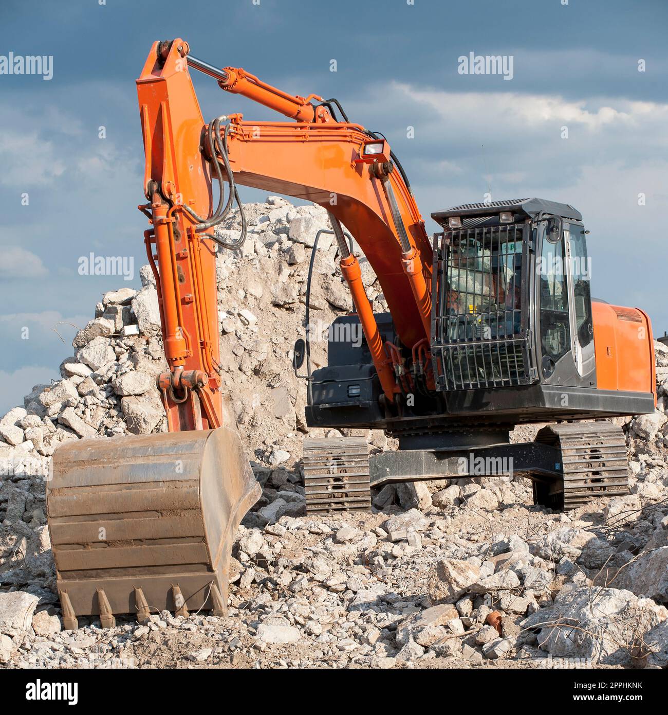 Square photo of an excavator with chain wheels and shovel standing on a pile of rubble without logos and other legal identifiers. Stock Photo