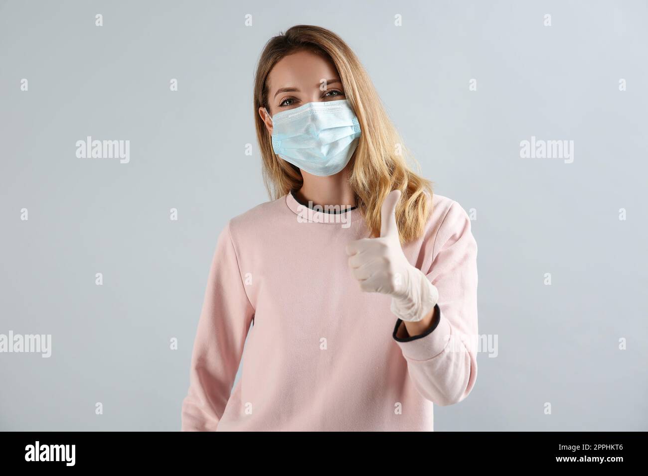 Young woman in medical gloves and protective mask showing thumb up on ...