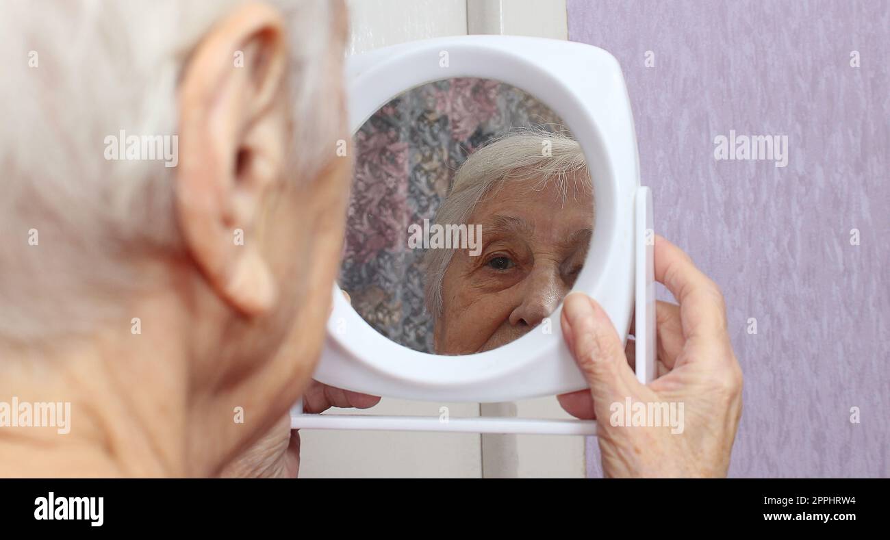 Portrait of old woman looking into a mirror at home Stock Photo