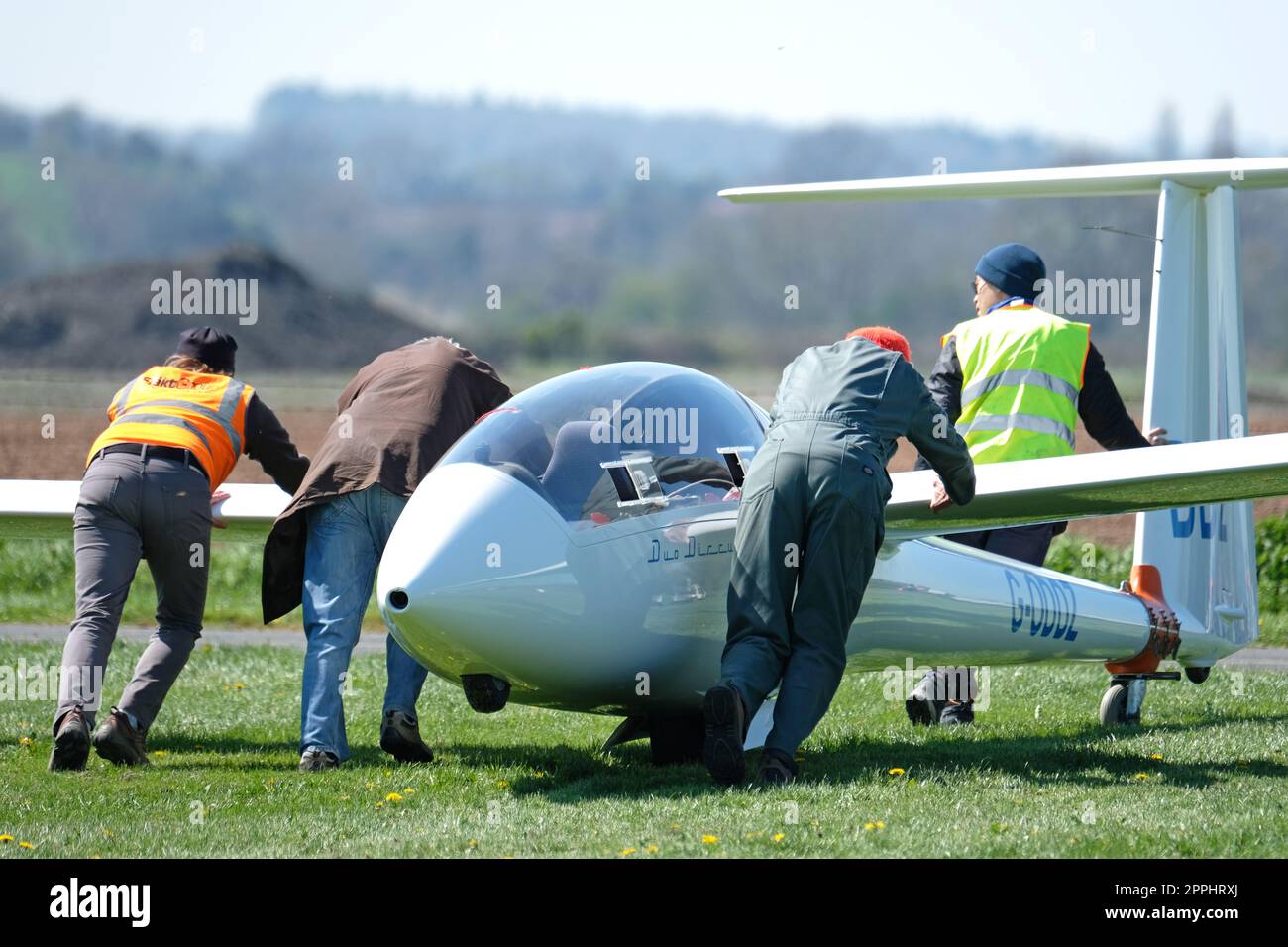 Team work as members of a gliding club move a glider across a grass airfield in the UK Stock Photo