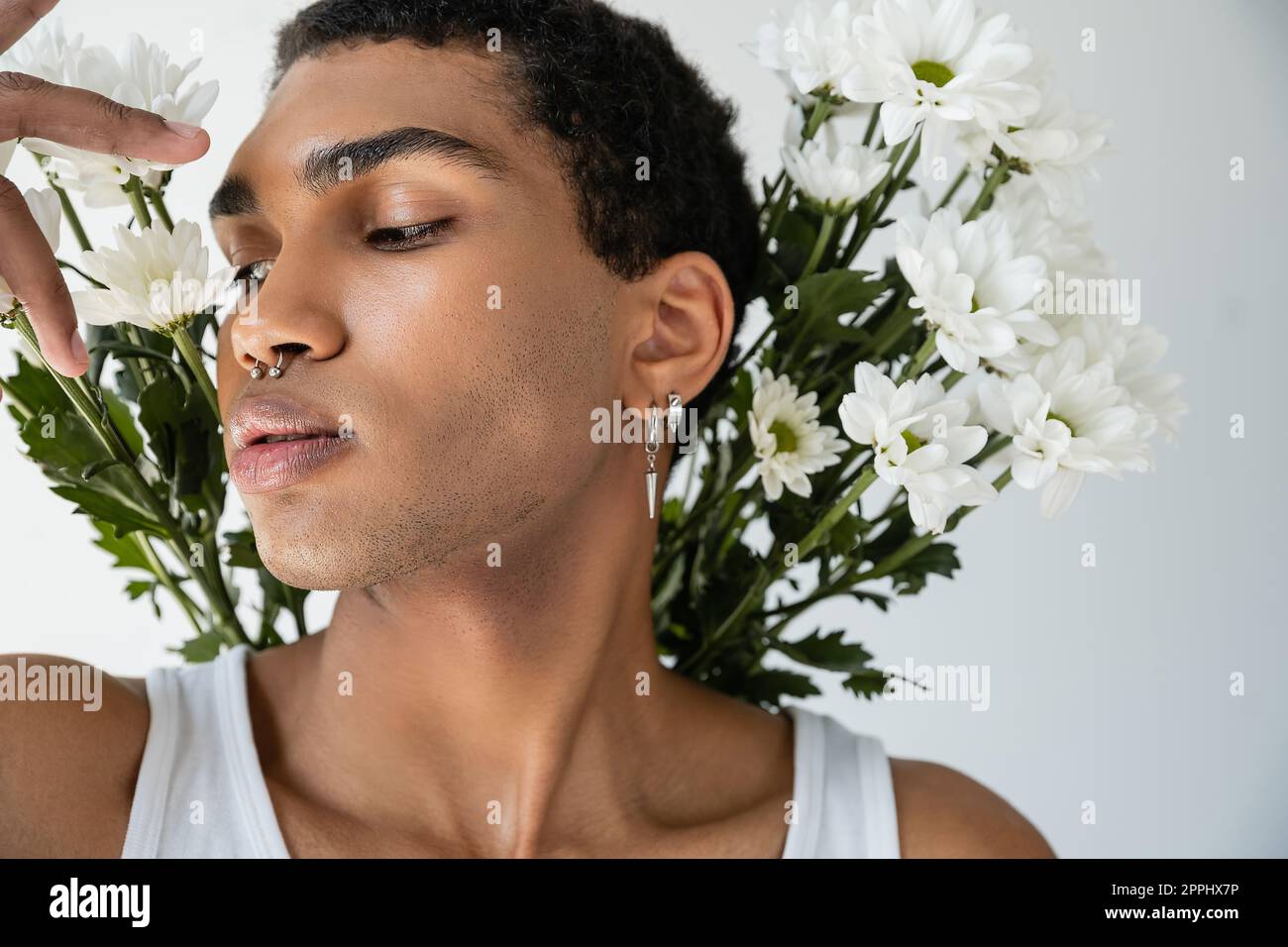 portrait of african american man with silver piercing posing near white fresh flowers isolated on grey,stock image Stock Photo
