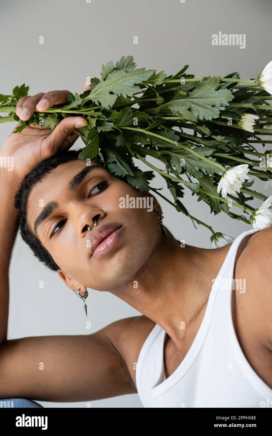 young african american man in white tank top posing with white chrysanthemums isolated on grey,stock image Stock Photo