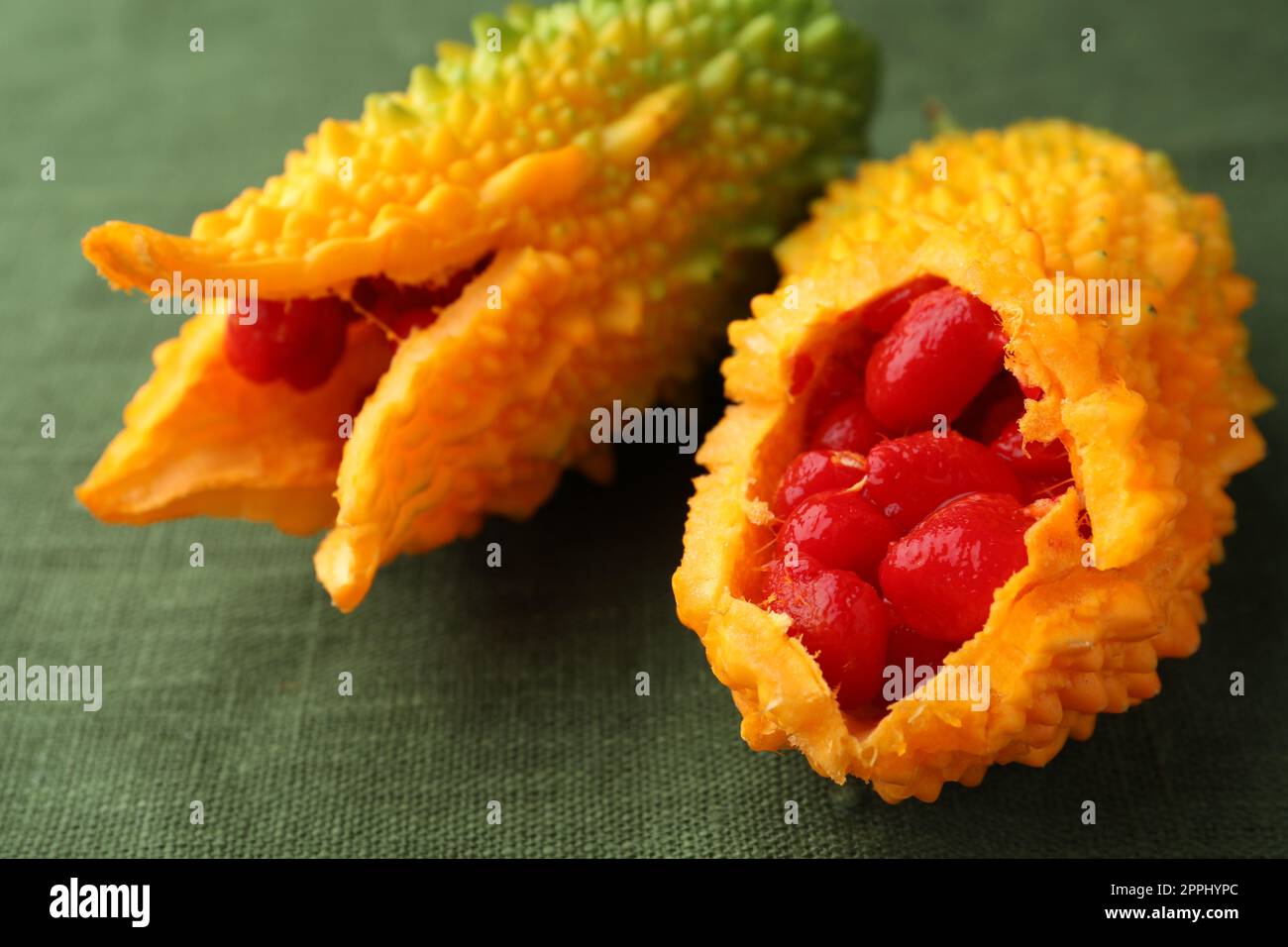 Fresh bitter melons with red seeds on dark green cloth, closeup Stock Photo