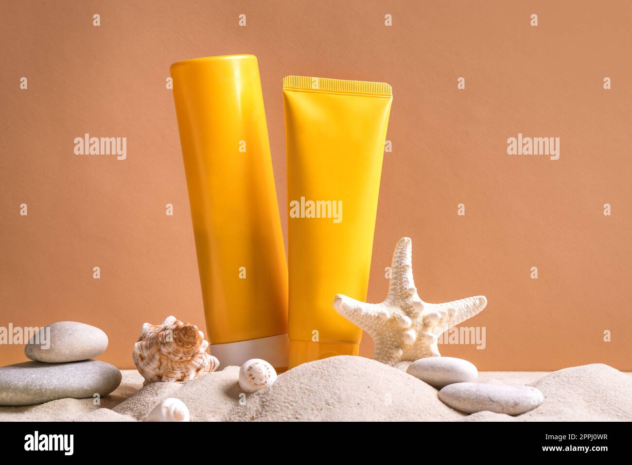 Sunblock in orange cosmetic tubes on beach sand and beige background, side view. Summer vacation and skin care concept with starfish and sea shells, s Stock Photo