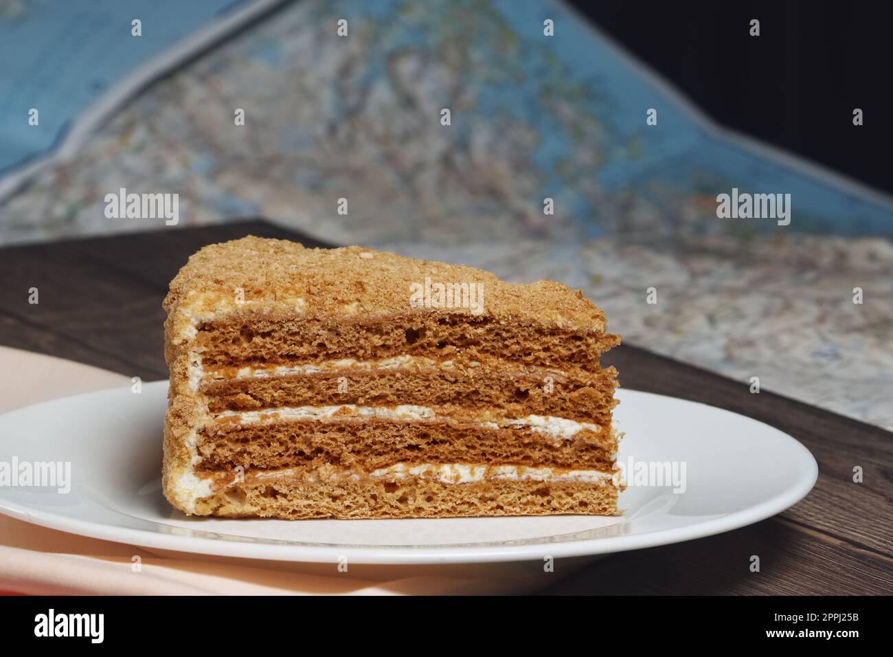 Piece of honey cake on plate near map on the table. Stock Photo