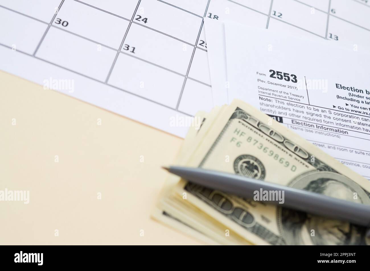 IRS Form 2553 Election by a Small Business Corporation tax blank lies with pen and many hundred dollar bills on calendar page Stock Photo