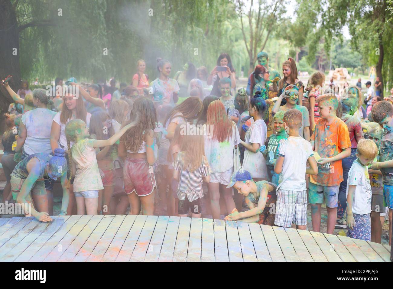 Lviv, Ukraine - July 18, 2021: Color Holi Festival, a crowd of people adults and small children throw colorful paint. Indian holiday, children running on a wooden stage, poor visibility due to paint dust. Stock Photo