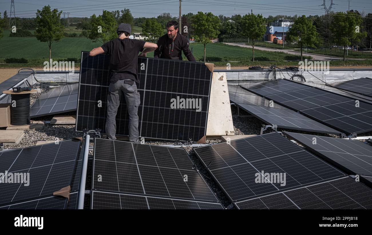 Male team engineers installing stand-alone solar photovoltaic panel system. Electricians mounting blue solar module on roof of modern house. Alternative energy concept Stock Photo