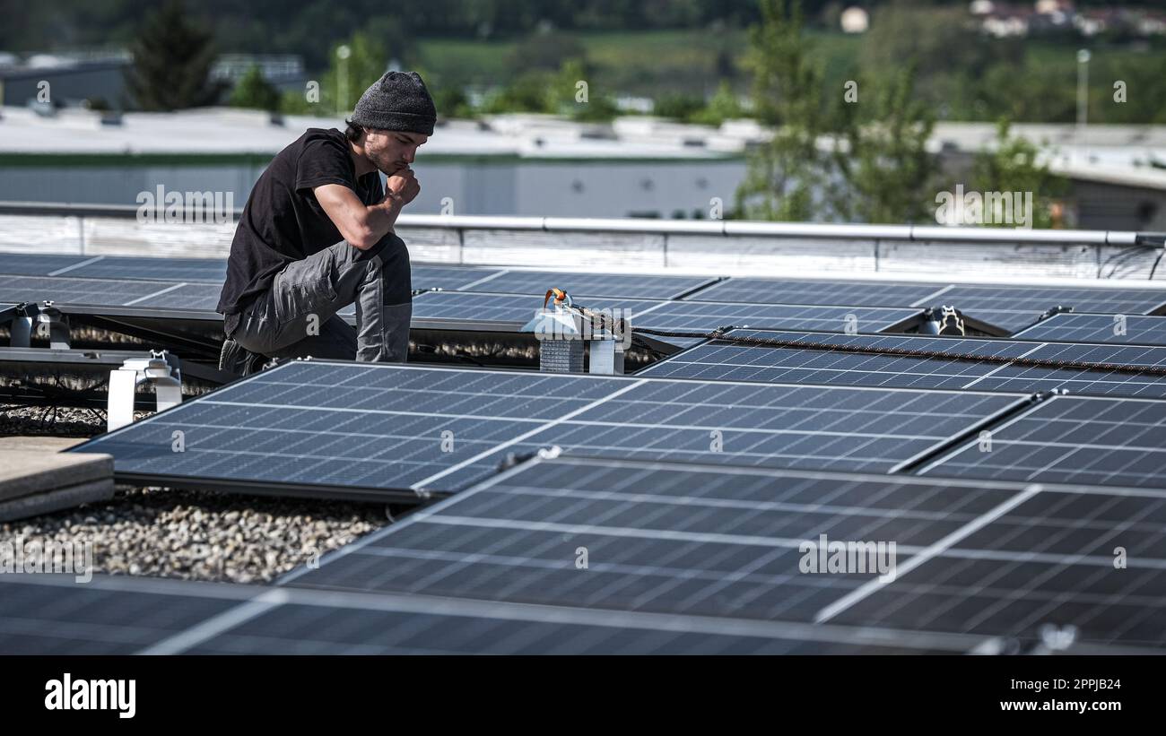 Male team engineers installing stand-alone solar photovoltaic panel system. Electricians mounting blue solar module on roof of modern house. Alternative energy concept Stock Photo