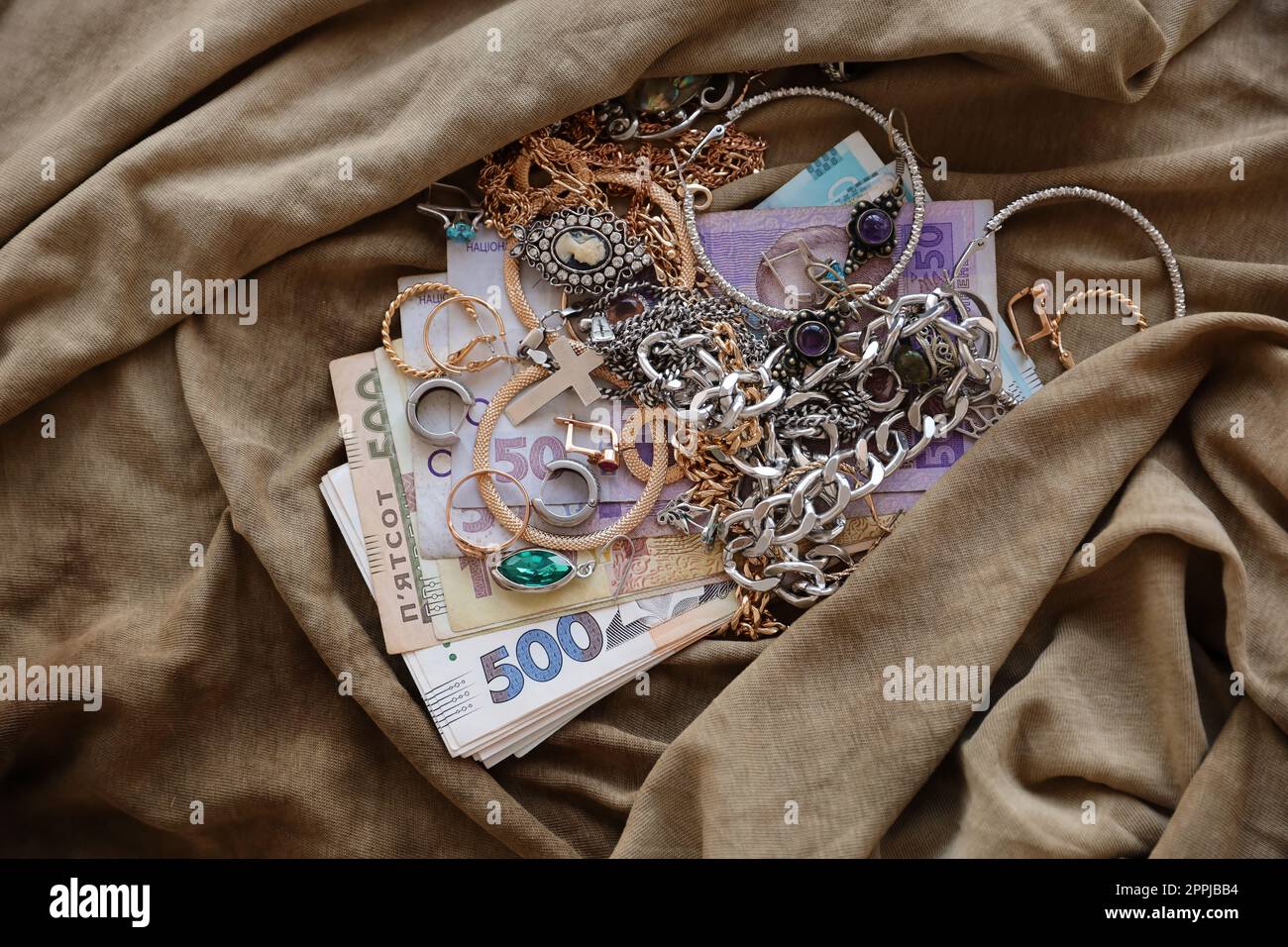Bunch of stolen jewelry and money on military uniform cloth fabric. Looting by Russian soldiers in the Ukrainian cities during the Russian attack on Ukraine. Marauders and looters Stock Photo