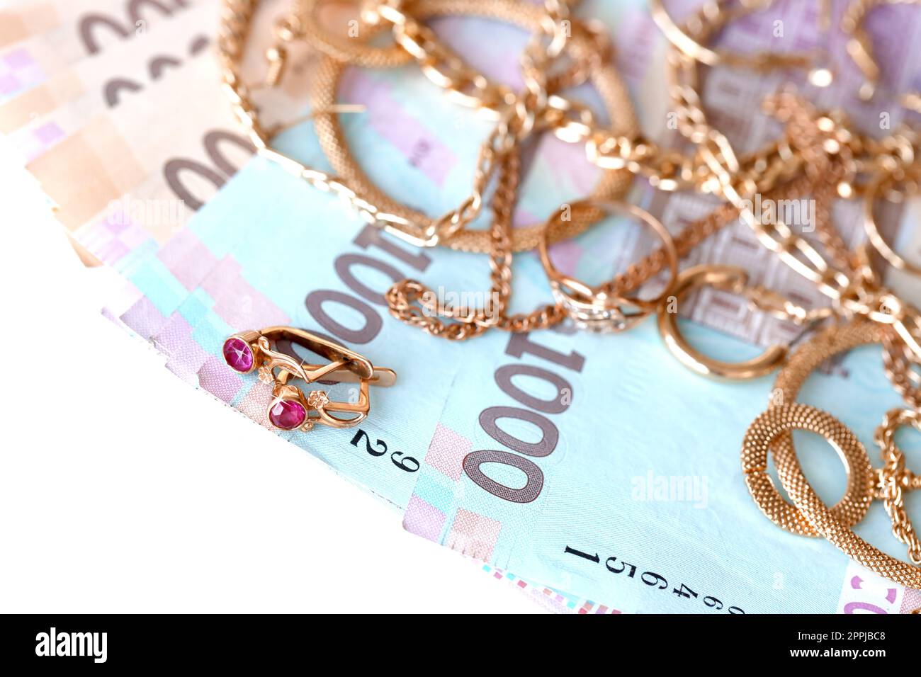 Many expensive golden jewerly rings, earrings and necklaces with big amount of Ukrainian money bills. Pawnshop or jewerly shop concept. Jewelry trading Stock Photo