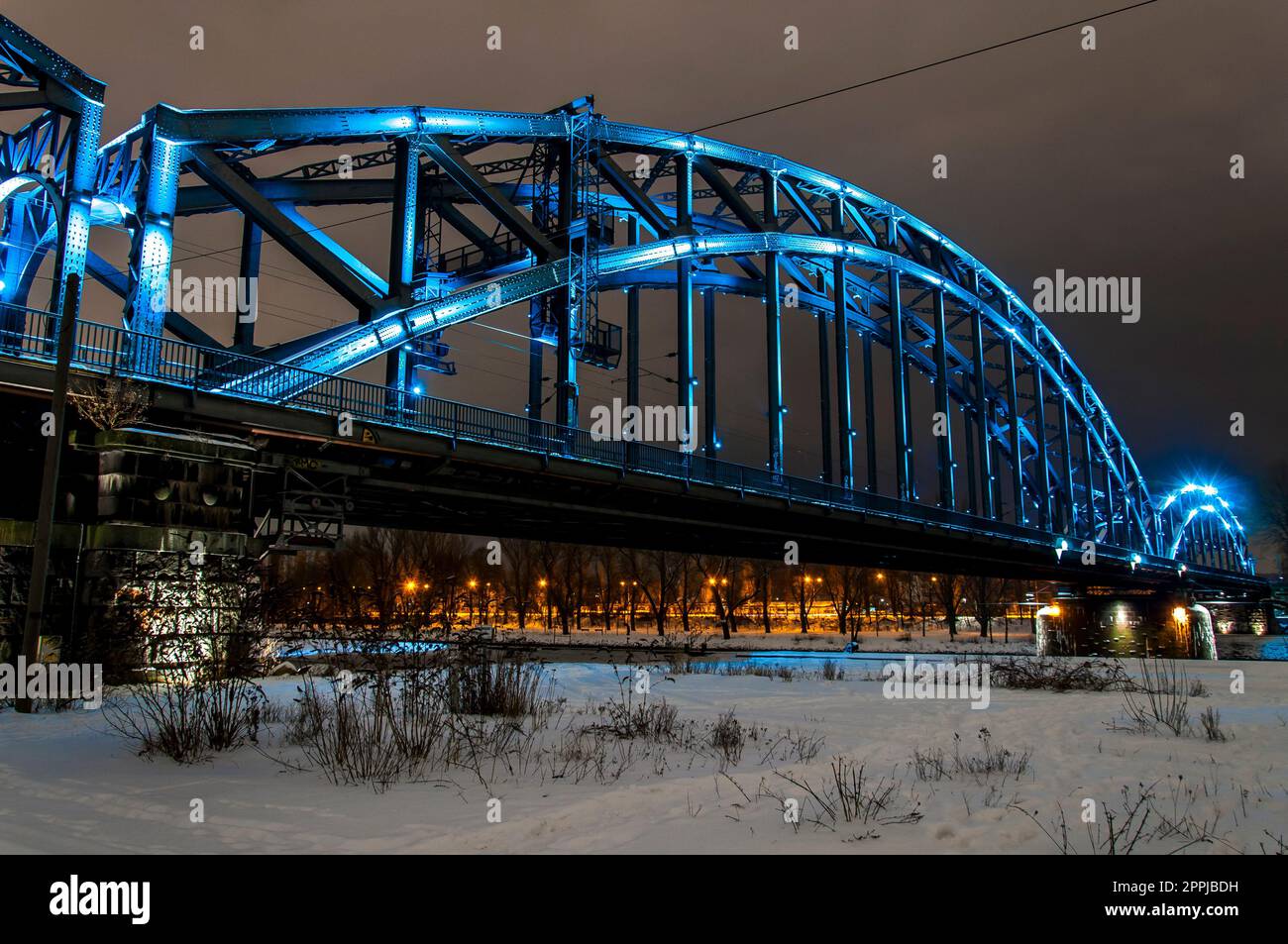 Blue illuminated steel arch bridge at night with snowy background Stock Photo