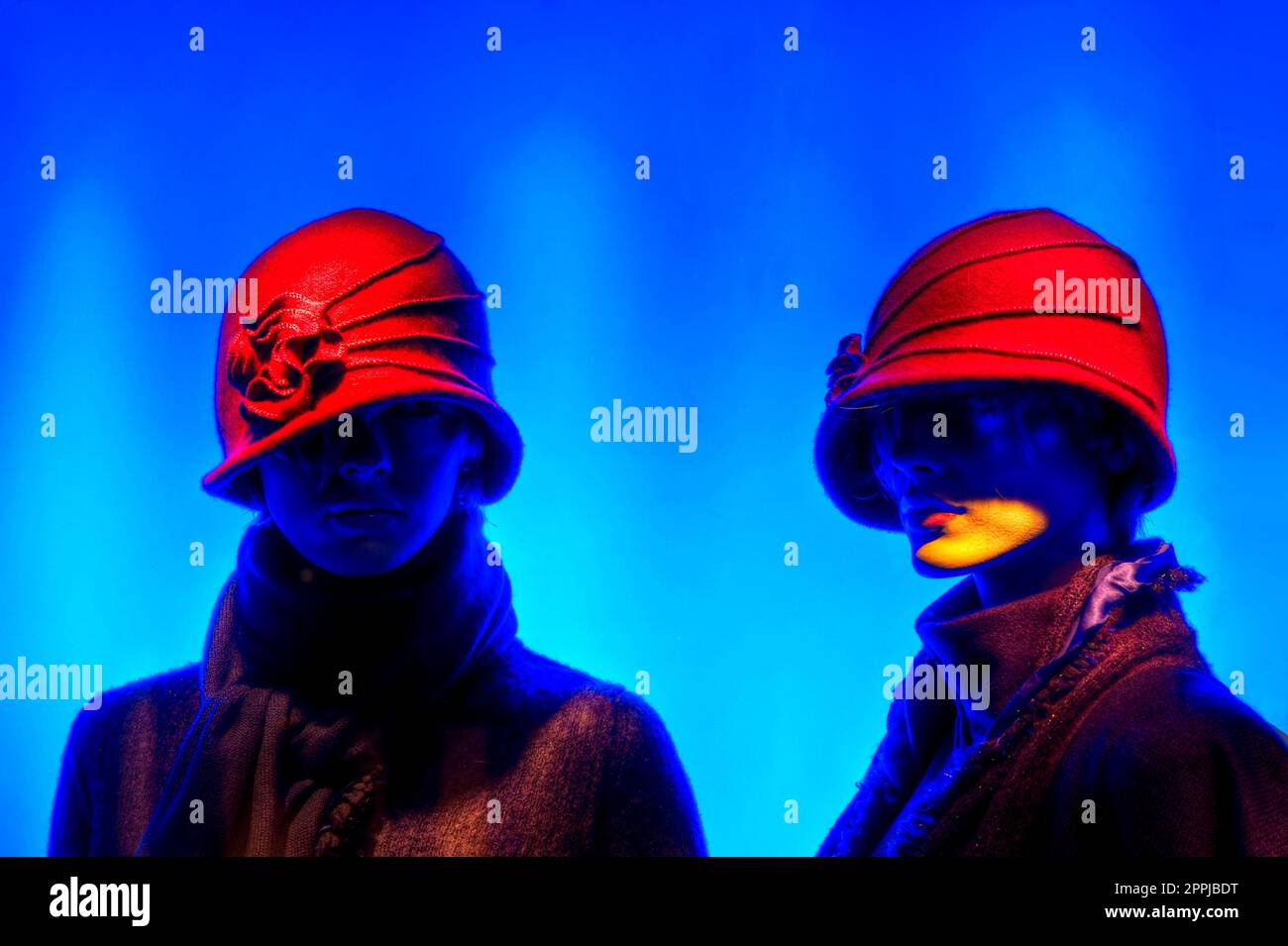 Two mannequins dressed in red hats against blue background Stock Photo