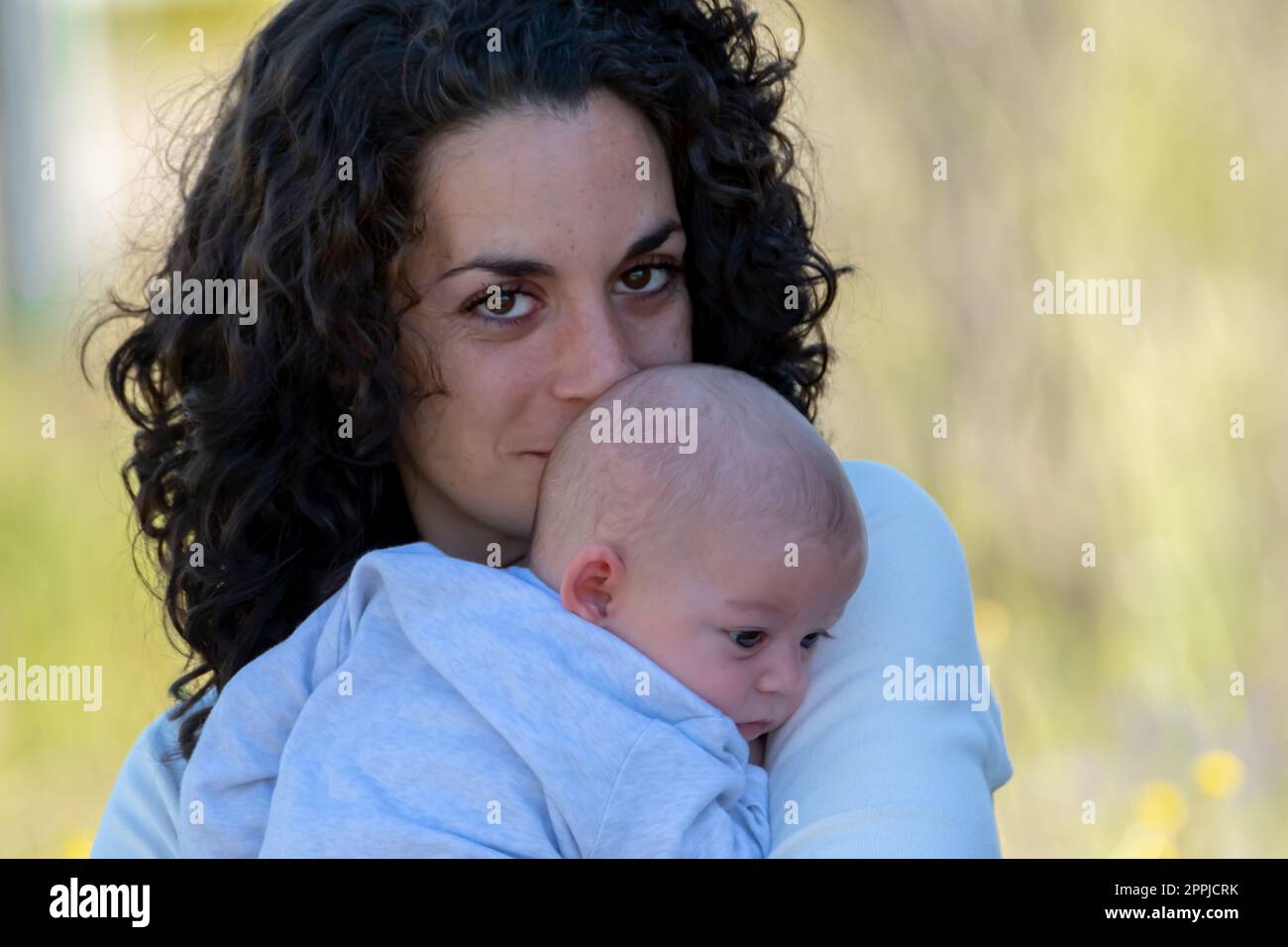 young mother with curly hair poses looking at camera while holding her newborn baby in her arms. family and newborn care concept. Stock Photo