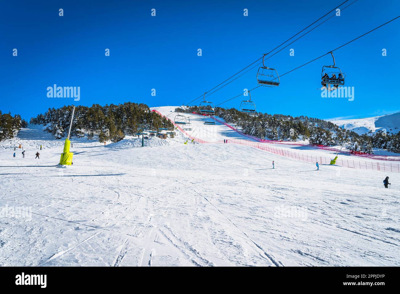 People riding up on a ski chair lift and skiing and snowboarding down on the ski slope, Andorra Stock Photo