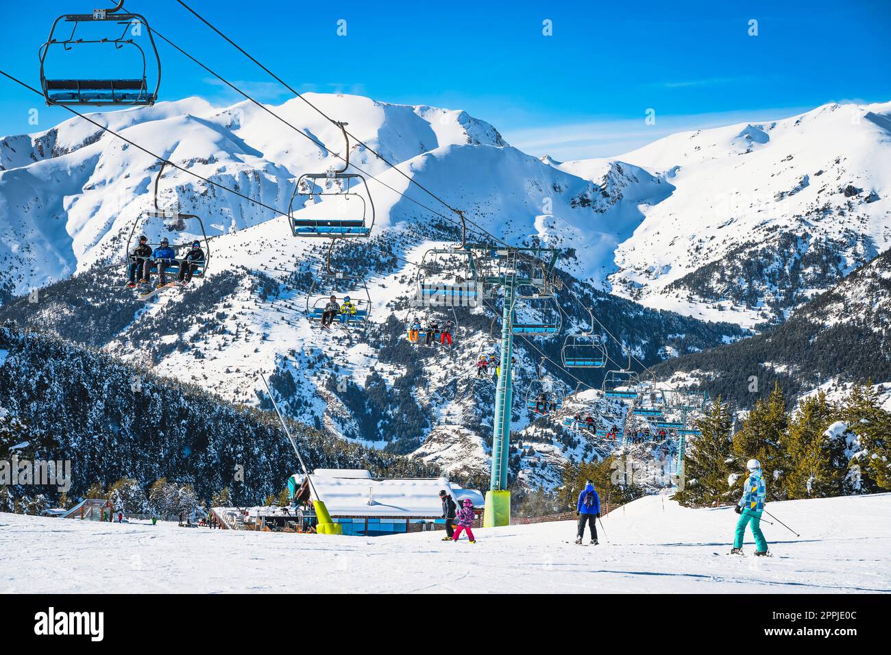 People riding up on a ski chair lift and skiing and snowboarding down on the ski slope, Andorra Stock Photo
