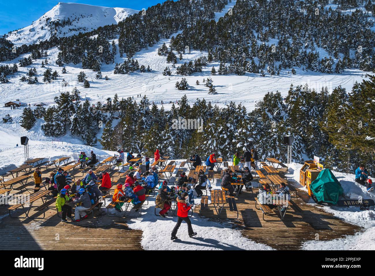 People sitting at the tables and relaxing with a beautiful view on snowy mountains and fores, Andorra Stock Photo