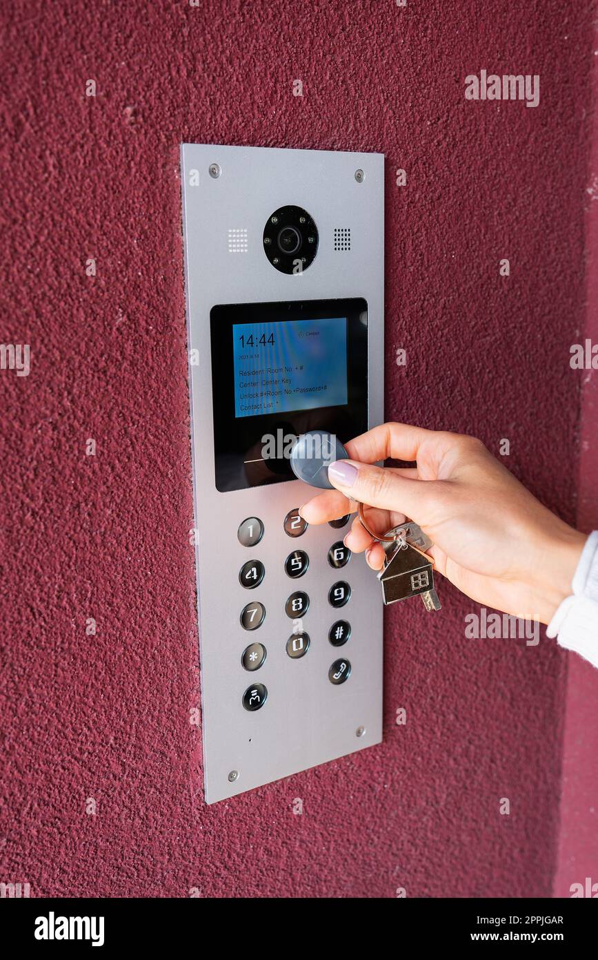 A young woman types the apartment code on the electronic intercom panel, opens the door with a touch key, the screen for viewing information. Protection and security concept. Stock Photo