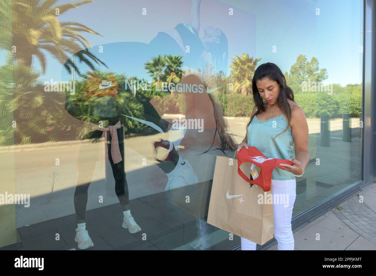 mallorca, balearic islands spain-november 05 2022: hispanic woman looking  at the window of the nike sports store happy comparing the purchase made in  the mall mallorca fashion outlet, on the outskirts of
