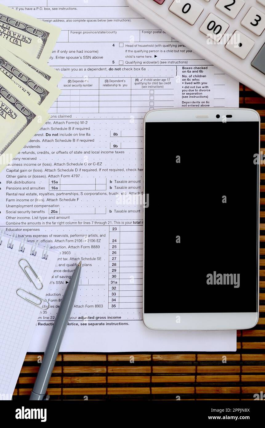 Composition of items lying on the 1040 tax form. Dollar bills, pen, calculator, smartphone, paper clip and notepad. The time to pay taxes Stock Photo