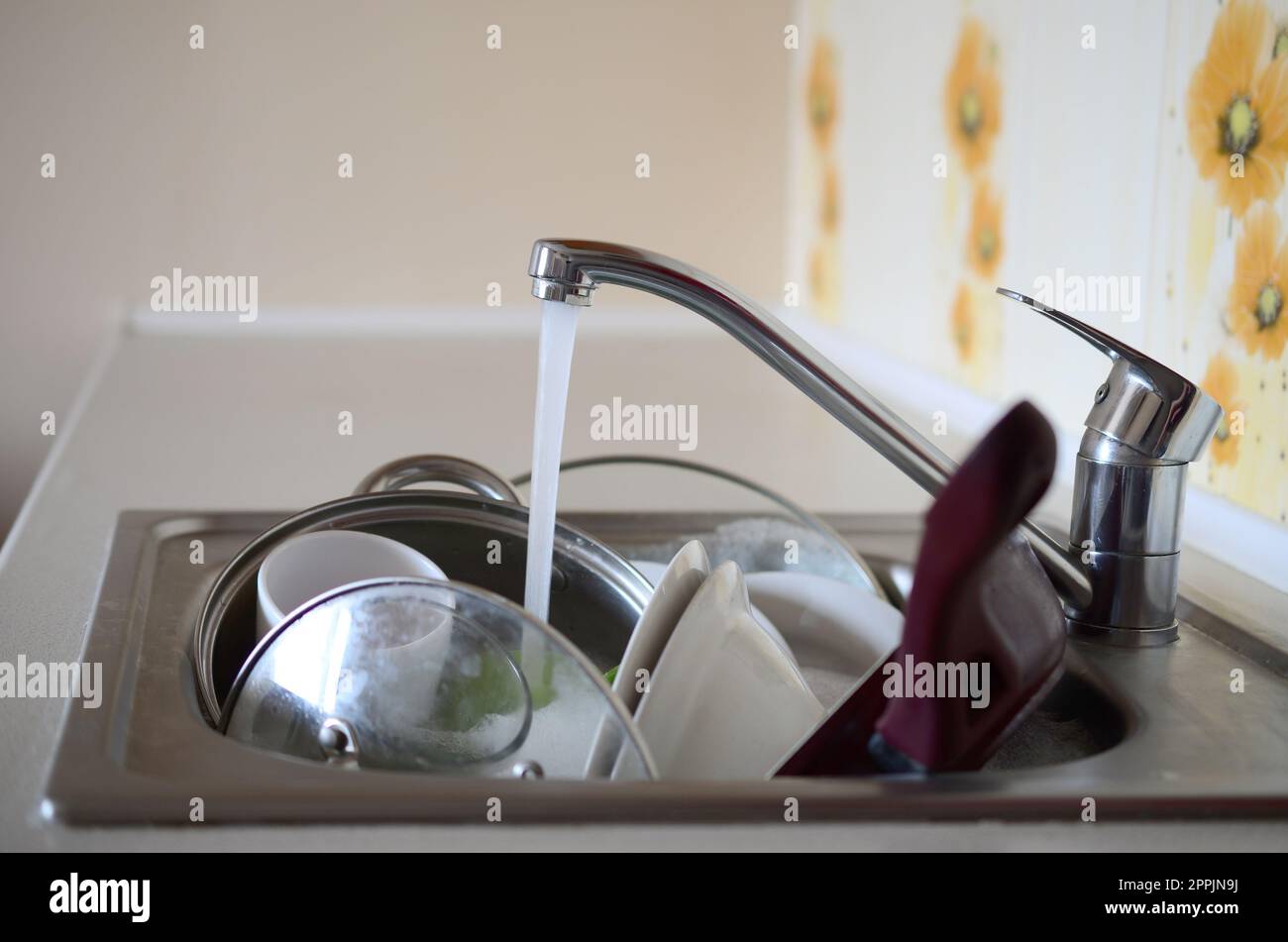 Dirty dishes and unwashed kitchen appliances lie in foam water under a